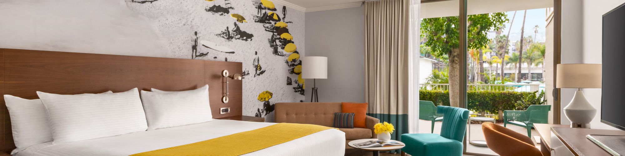 A modern hotel room with a large bed, stylish wall art, comfortable seating area, and a window overlooking a green outdoor space ends the sentence.