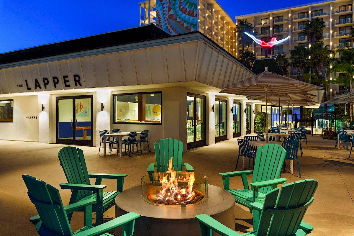 The image shows an outdoor seating area at night with green chairs around a fire pit, near a building labeled "The Lapper."