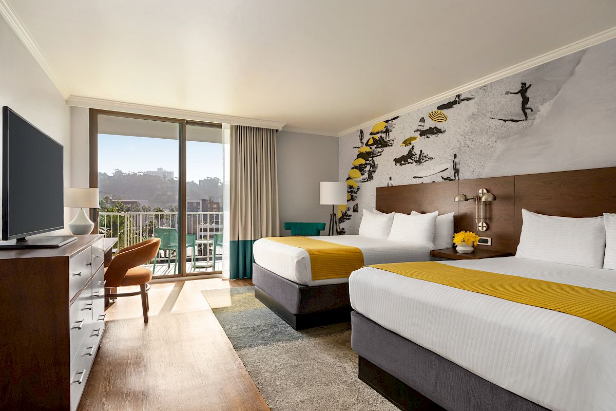 A modern hotel room with two double beds, a large window with a balcony, wall art, a TV, and a desk with a chair.