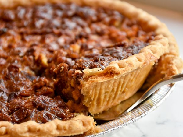 The image shows a close-up of a pecan pie with a slice being cut out, revealing a rich, nutty filling.
