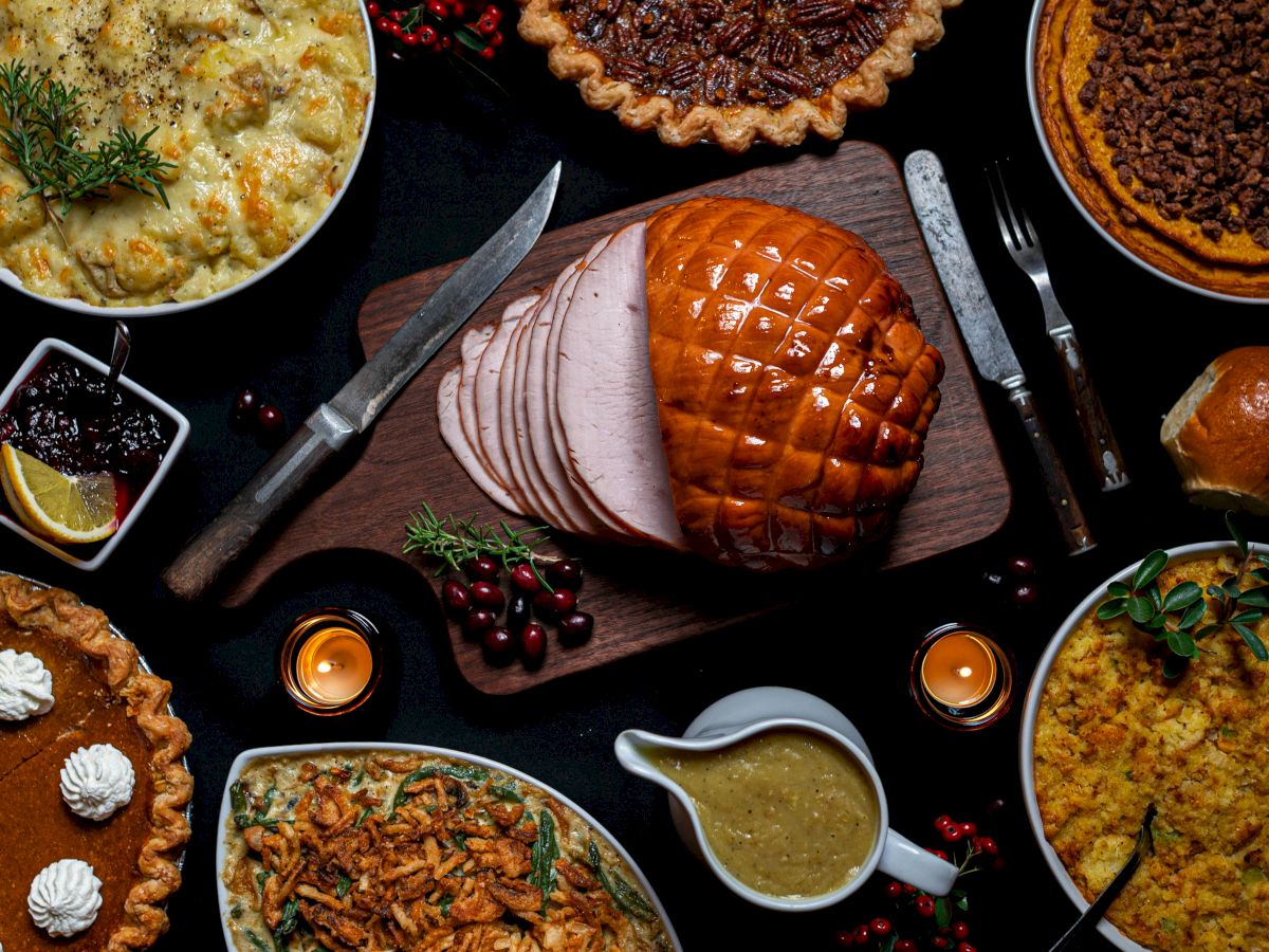 A festive spread of sliced roast meat, pies, casseroles, gravy, and vegetables on a dark tabletop.
