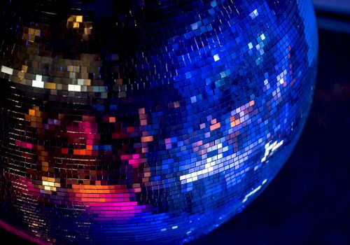 The image shows a close-up of a shiny disco ball reflecting colorful lights in a dark environment.