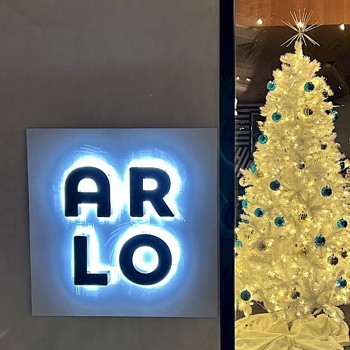A neon sign reading "ARLO" is on the left, and a white Christmas tree with blue ornaments is on the right.