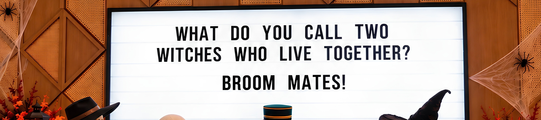 A Halloween stage: costumed witches and a masked bride surround a screen reading, &ldquo;What do you call two witches who live together? Broom mates!&rdquo;