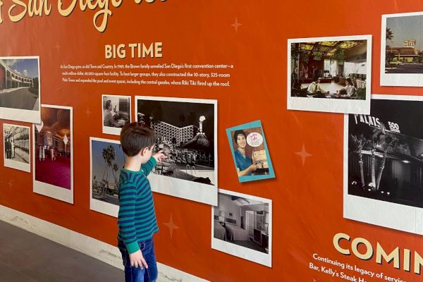 A child looks at a wall display about Town and Country Resort, a San Diego icon since 1953, with historical photos and text.