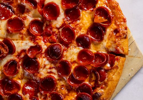 A pepperoni pizza on a wooden pizza peel, with melted cheese and crispy pepperoni slices, sits on a marble surface.