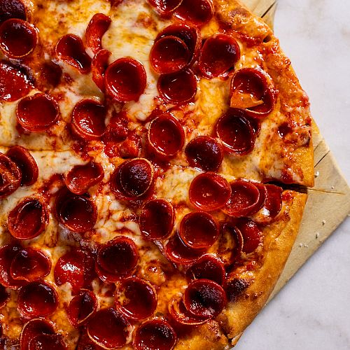 A pepperoni pizza on a wooden pizza peel, with melted cheese and crispy pepperoni slices, sits on a marble surface.