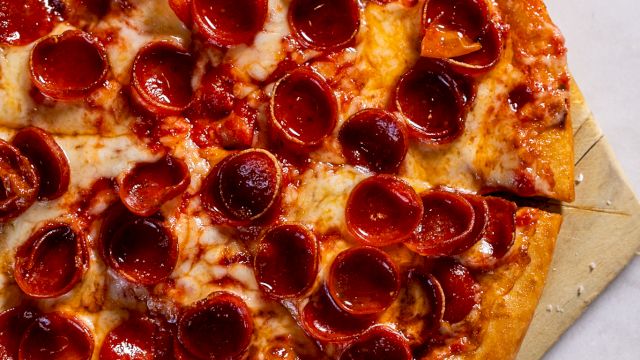 A pepperoni pizza on a wooden pizza peel, with melted cheese and crispy pepperoni slices, sits on a marble surface.