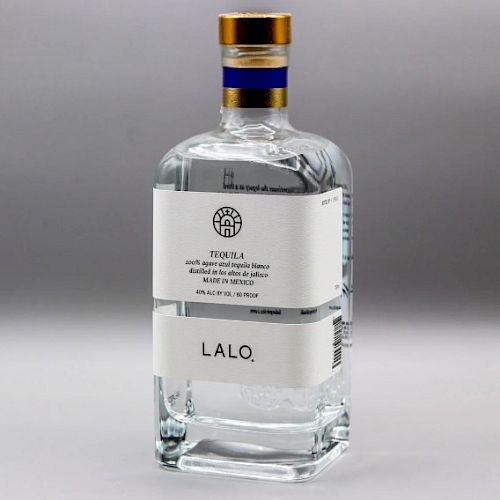 This image shows a bottle of LALO tequila, featuring a white label and a gold cap with a blue stripe, set against a neutral background.