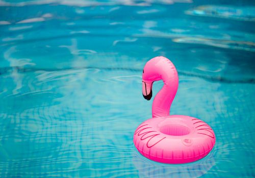 A pink flamingo pool float is floating in a clear blue swimming pool.