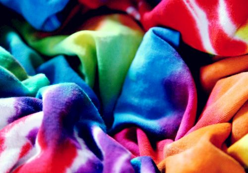A colorful tie-dye fabric is crumpled, showcasing vibrant patterns and hues of blue, red, green, and orange in the image.