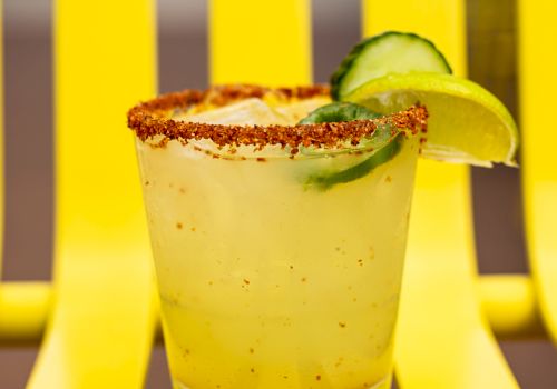 A yellow drink with a chili-rimmed glass, garnished with lime and cucumber, placed on a matching yellow chair for a vibrant look.