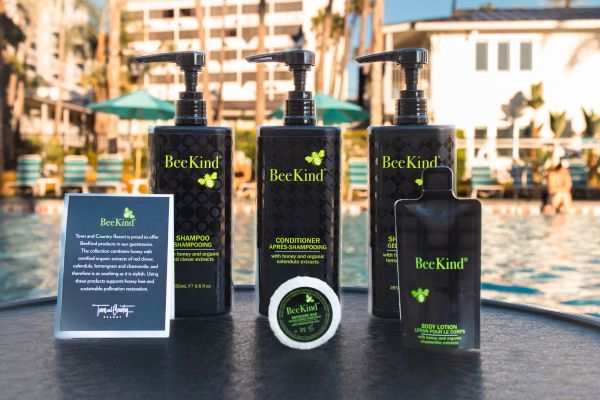 BeeKind shampoo, conditioner, lotion, and soap displayed by a pool, with a BeeKind information card beside them.