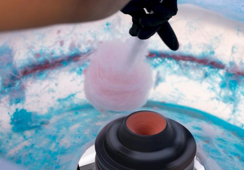 A person is making pink cotton candy in a machine, with blue and pink sugar residue visible inside.