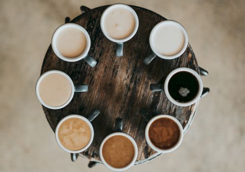 A round table with eight mugs of coffee, each varying in color and intensity, arranged in a circle.