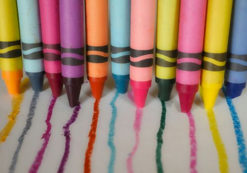 Colorful crayons are lined up in a row, each drawing a line in matching color on a white surface.