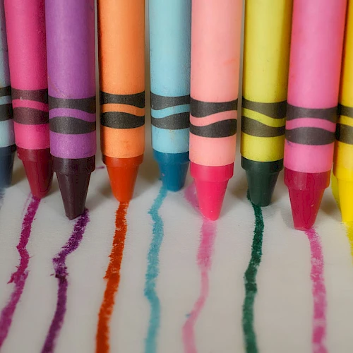 Colorful crayons are lined up in a row, each drawing a line in matching color on a white surface.