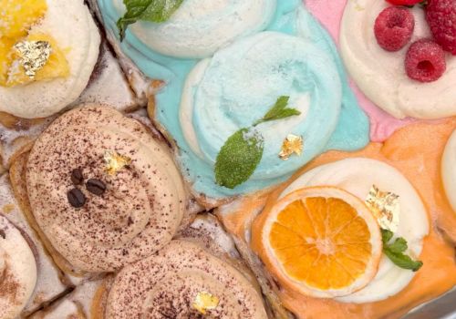 A variety of ice creams with colorful flavors and toppings like fruit slices, mint leaves, and chocolate shavings are displayed.