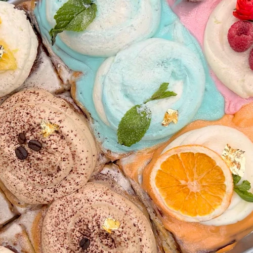 A variety of ice creams with colorful flavors and toppings like fruit slices, mint leaves, and chocolate shavings are displayed.