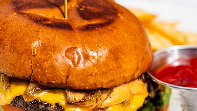A cheeseburger with lettuce and tomato, served on a plate with a side of fries and ketchup.