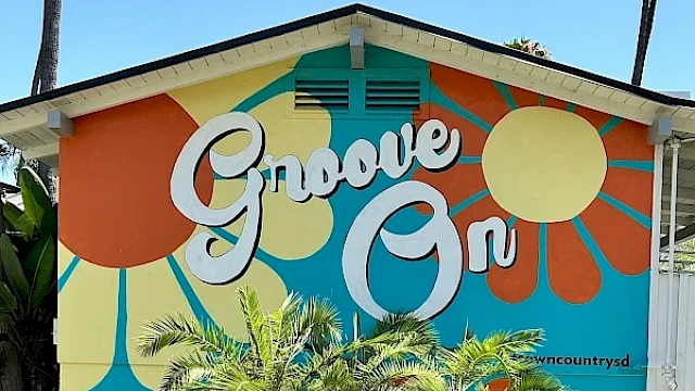 A colorful mural on a building reads "Groove On" with retro-style design elements and palm trees in the foreground.