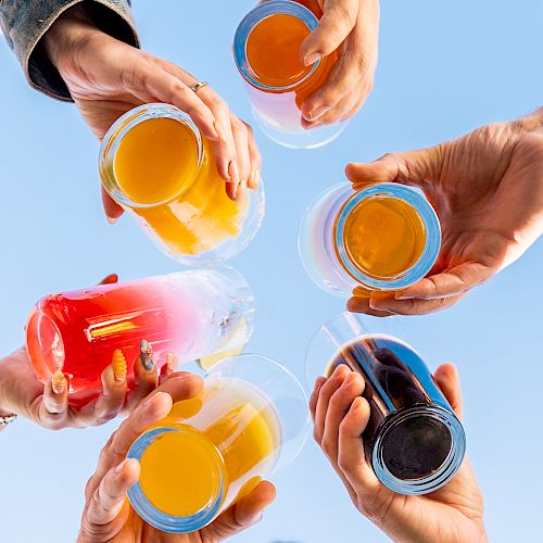 People are raising a variety of colorful drinks into the sky in a celebratory gesture.