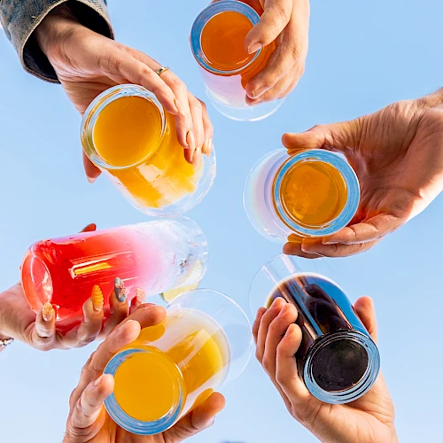 People are raising a variety of colorful drinks into the sky in a celebratory gesture.