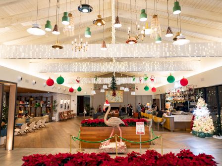 An indoor holiday restaurant lobby with hanging lamps and lights, Christmas ornaments, and a decorated flamingo in front.