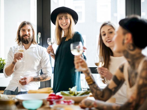 A group of four people enjoying a casual gathering, smiling and holding glasses, in a bright, modern room with a table of food.