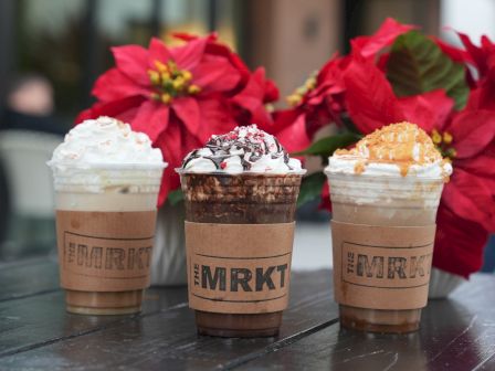 Three iced coffees topped with whipped cream sit on a table, with festive red poinsettias in the background.