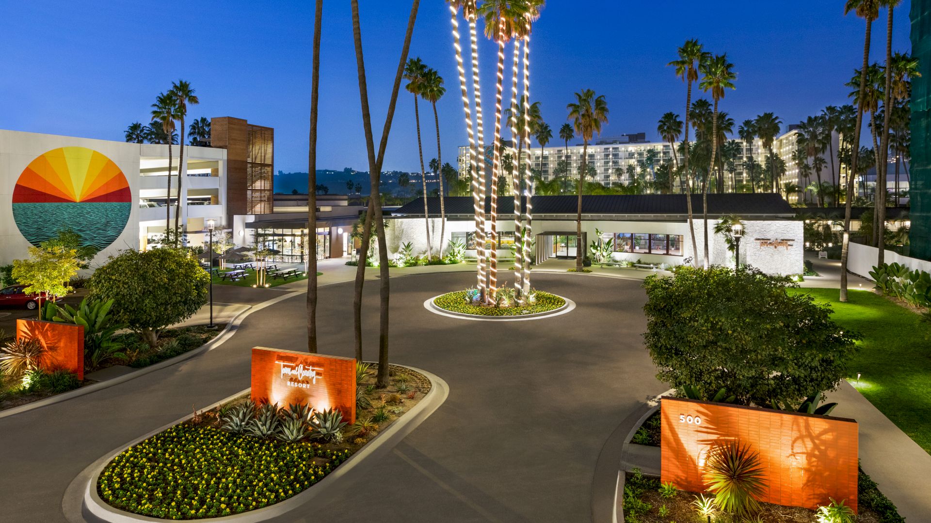 This image shows a building with palm trees and a circular driveway, set against a twilight sky.