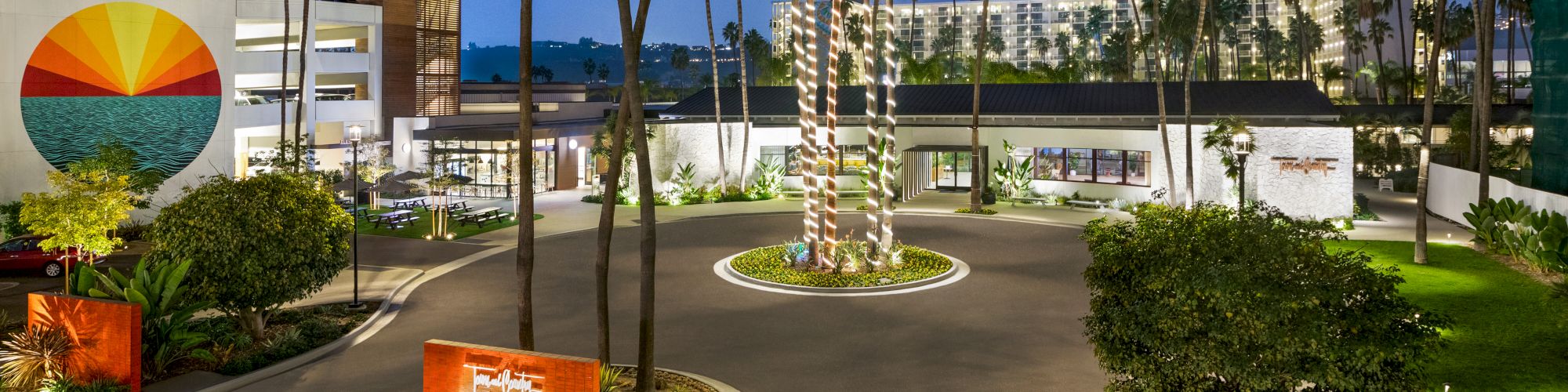 This image shows a building with palm trees and a circular driveway, set against a twilight sky.