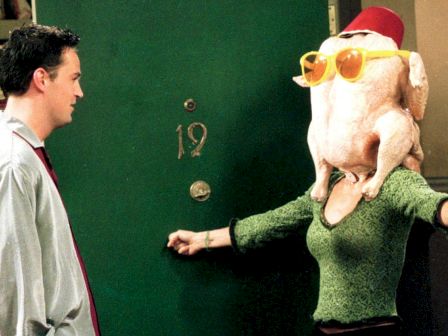 A person with a turkey on their head stands by a door marked "19," next to another person. The turkey is wearing sunglasses and a hat.