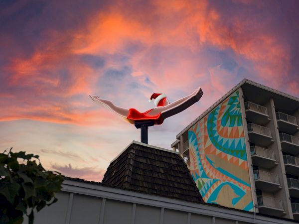 A vibrant sky at sunset behind a rooftop sculpture of a swimmer diving alongside a mural on a tall building.